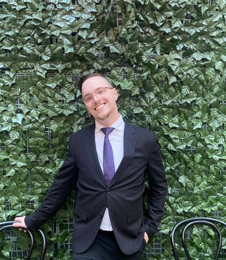 Patrick Braley, professional hypnotist and performer, in a suit against an ivy wall.